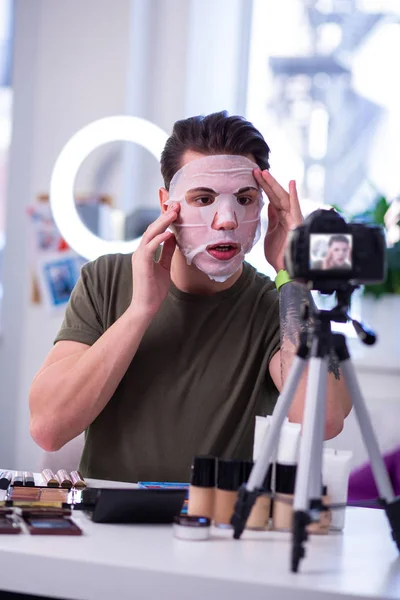 Expresivní neobvyklý muž ošetřující jeho kůži pečlivou tkáňové maskou — Stock fotografie