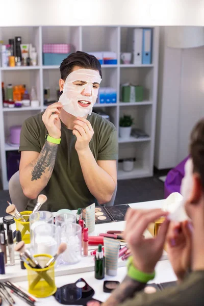 Tmavovlasý chlapík, který si při sezení ve studiu krásy bere obličejovou masku — Stock fotografie