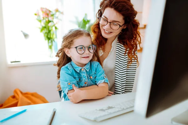 Дочка дивиться на екран комп'ютера, що приєднується до матері на роботі — стокове фото