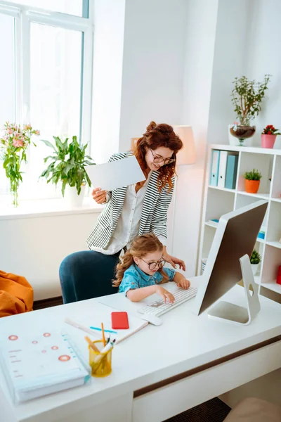 Legrační dcera používající klávesnici při připojení k matce v práci — Stock fotografie