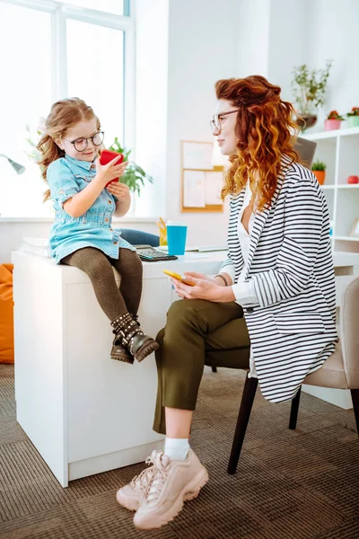 Freelancer elegante olhando para sua filha engraçada usando smartphone — Fotografia de Stock