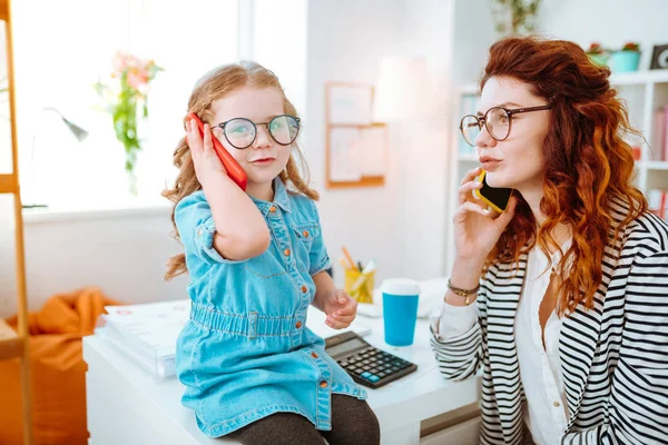 Linda hija repitiendo después de la madre mientras pone el teléfono cerca de la oreja — Foto de Stock