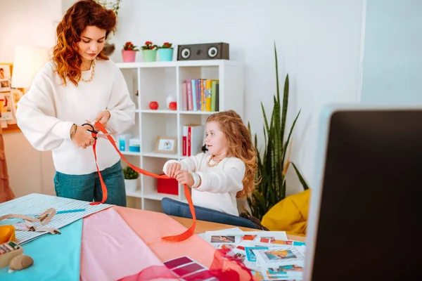 Diseñadora de moda cortando cinta roja con su niña ayudándola — Foto de Stock