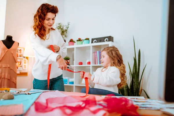 Chica ayudando a su mamá a diseñar ropa y cortar cinta — Foto de Stock