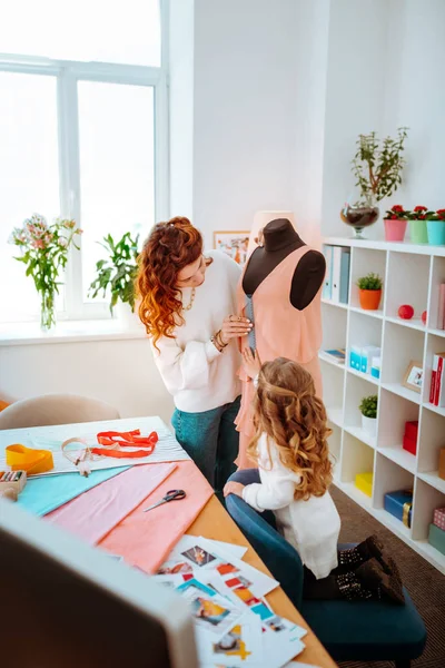 Designer standing near dress form with her little daughter