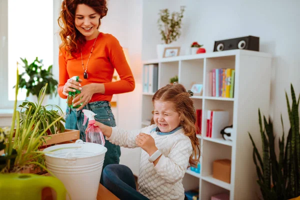 Chica alegre haciendo cara divertida después de rociar agua en la planta casera —  Fotos de Stock