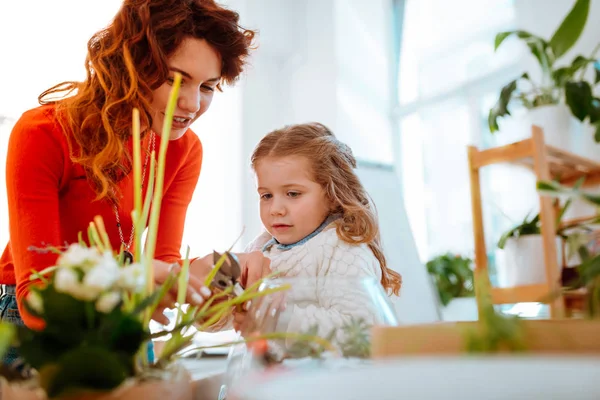 Mãe de cabelos vermelhos cortando bordas secas de planta em casa com filha — Fotografia de Stock