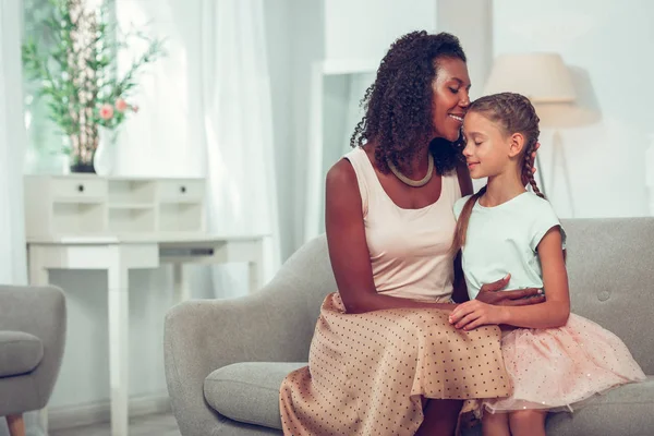 Encantadora madre afro-americana cariñosa abrazando tiernamente a la pequeña hija bastante dulce — Foto de Stock