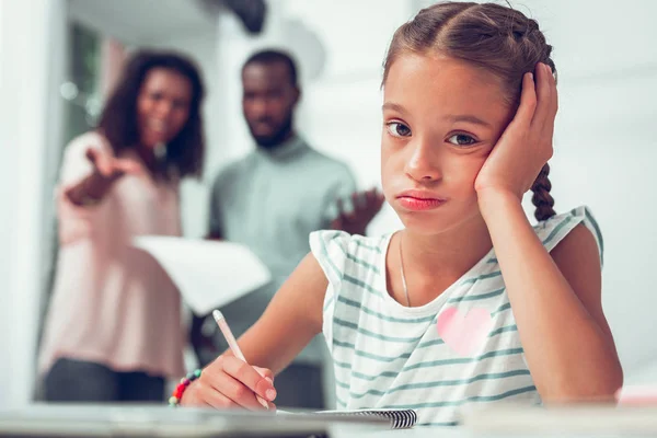 Retrato facial de una chica haciendo lecciones cuando sus padres hablan — Foto de Stock