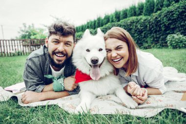 Samoyed ile çim üzerinde yatan çiftin yüz portresi.