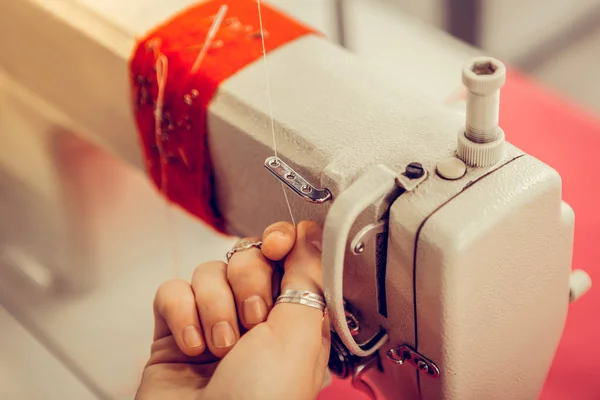 Mano de una modista insertando hilo en la máquina de coser . — Foto de Stock