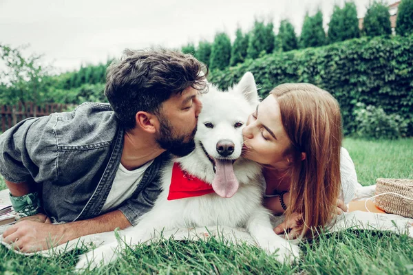 Gesichtsporträt eines schönen Paares, das liebevoll einen flauschigen Hund küsst. — Stockfoto