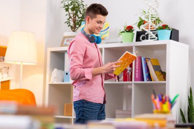 Kitaplık yanında duran ve okumak için kitap seçerek öğrenci