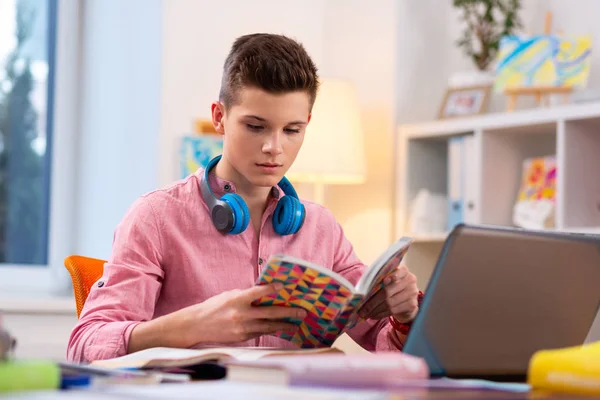 Подросток в наушниках на шее сидит за ноутбуком и учится — стоковое фото