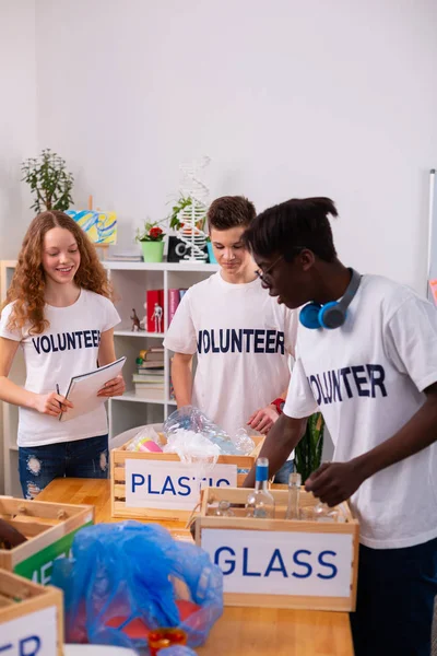 Tieners in witte t-shirts sorteren van glas en kunststof samen — Stockfoto