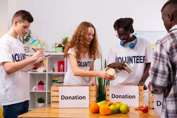 Cuatro adolescentes responsables poniendo comida en cajas para donación —  Fotos de Stock