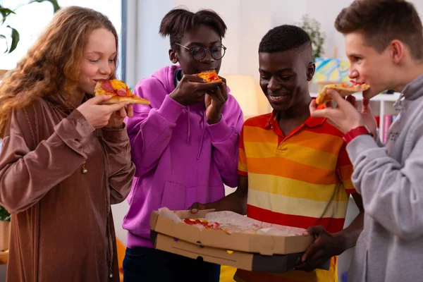 Cuatro adolescentes elegantes comiendo deliciosa pizza después de la escuela —  Fotos de Stock