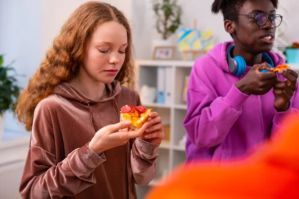 黒い肌の友人の近くに立ってペパロニとピザを食べる女の子 — ストック写真