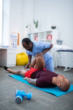 Bald sporcu mat üzerinde yatan ve bacaklar için fizik tedavi olan