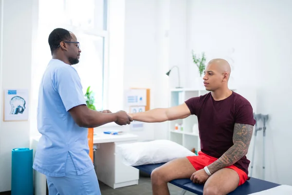 Sportsman with nice biceps visiting therapist after getting injury