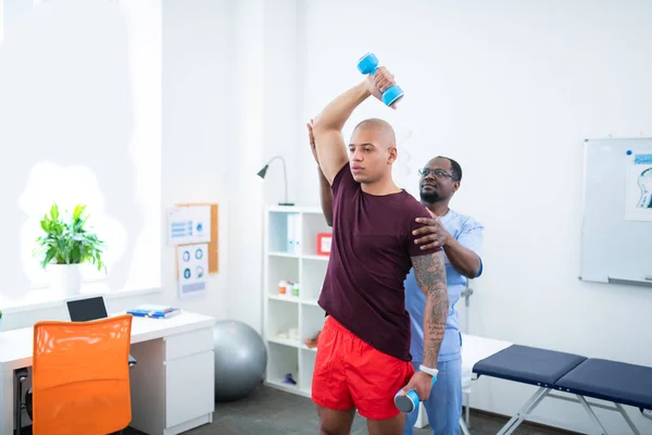 Man with nice muscles doing exercises visiting sports therapist