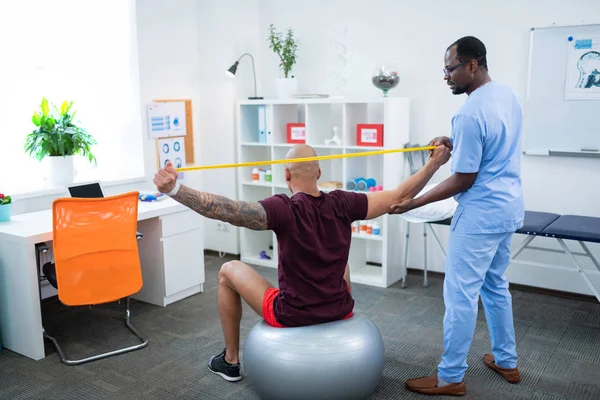 Kopasz ember csinál nyúlik vissza látogató fizikai terapeuta — Stock Fotó