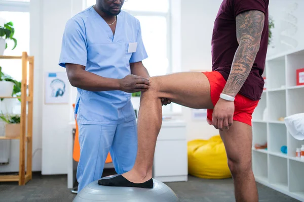 Deportista tatuado poner la pierna en la bola en forma mientras visita a terapeuta — Foto de Stock