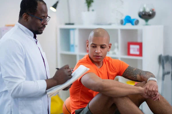 Татуйований спортсмен слухає свого лікаря після травми — стокове фото