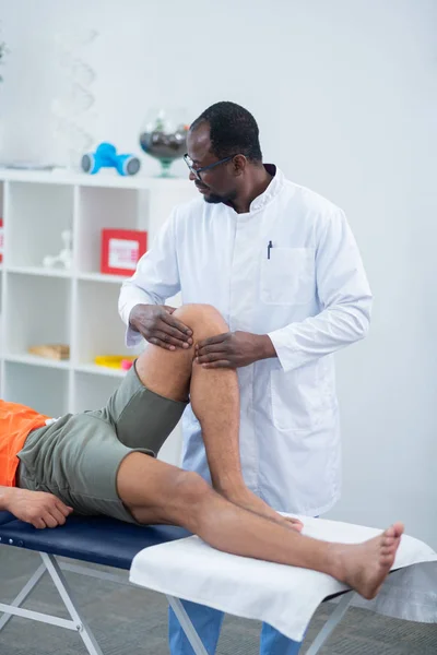 A terapeuta a fehér kabát ellenőrzése térd és láb a sportember — Stock Fotó