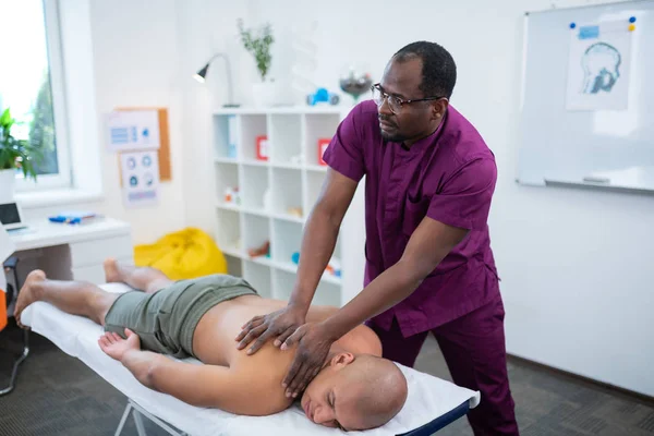 Темношкірий майстер масажу в уніформі відчуває себе зайнятим на роботі — стокове фото