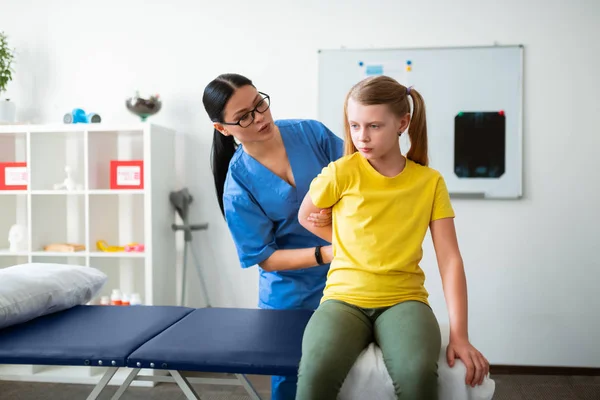 Enfant aux cheveux longs sérieux bougeant ses mains avec l'aide du médecin — Photo