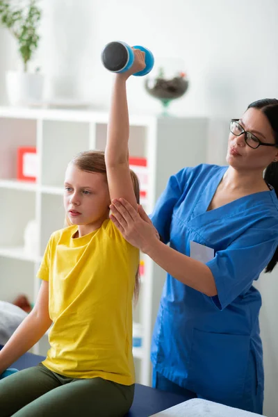 Orgulhoso satisfeito médico controlando procedimento enquanto criança levantando halteres — Fotografia de Stock