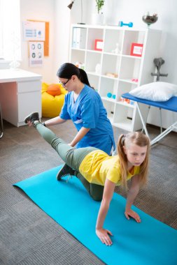 Dikkatli koyu saçlı fizyoterapist eğitim kız bacak tutan