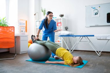 Profesyonel koyu saçlı terapist germe ile küçük kız yardım