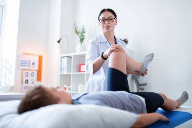 Beyaz cüppe nazik iyi görünümlü uzman çocuğun bacak yükselterek