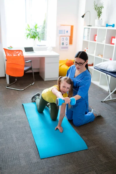 Chica joven seria criando pesadas mancuernas mientras está sentado en la esterilla de yoga — Foto de Stock