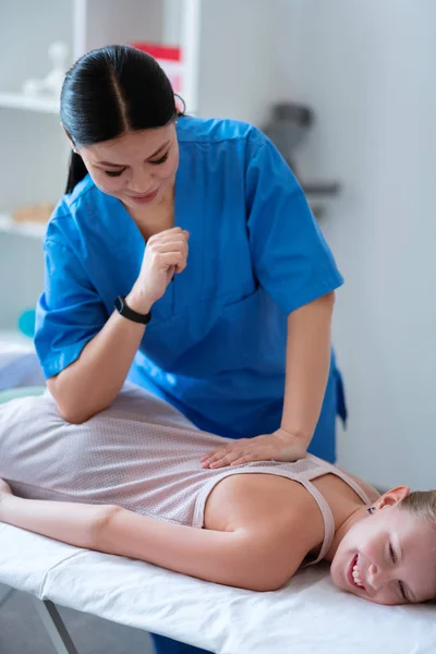 Agradável mestre de cabelos escuros em uniforme azul usando seu cotovelo durante a massagem — Fotografia de Stock