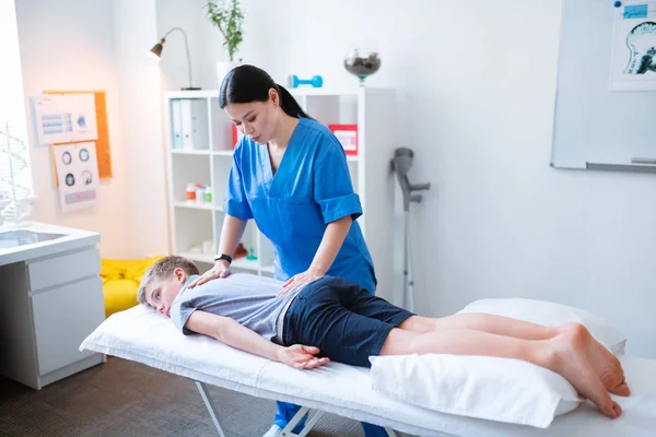 Langharige vrouw werken met rug van liggend jongetje — Stockfoto