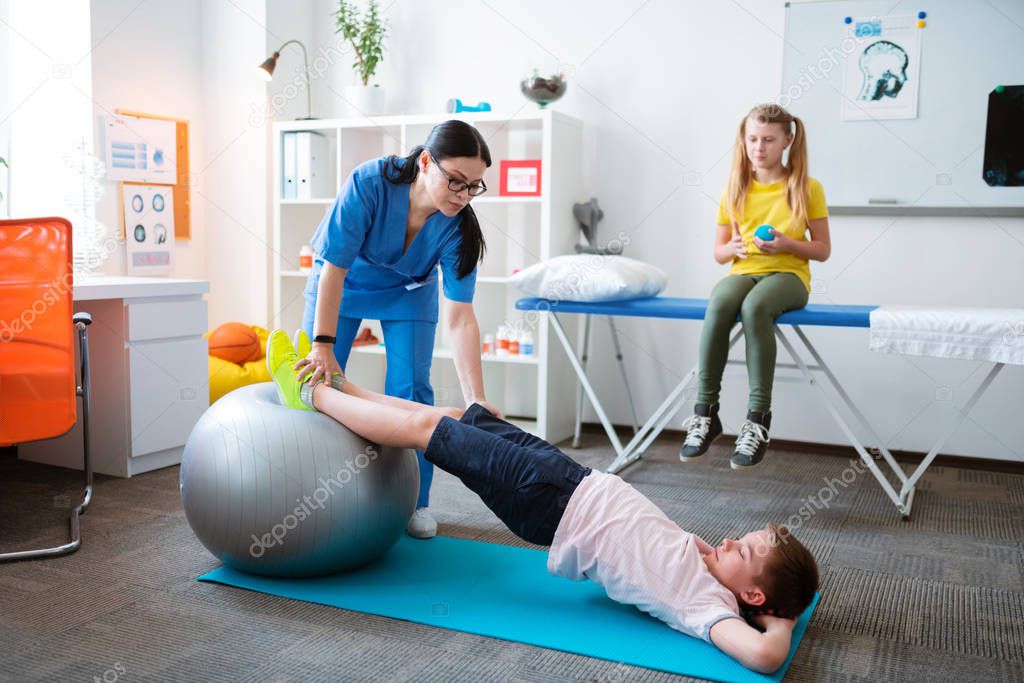 Active little patient stretching whole body while leaning on pilates ball