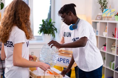 Büyük plastik şişe tutan boyun kulaklık ile koyu tenli genç
