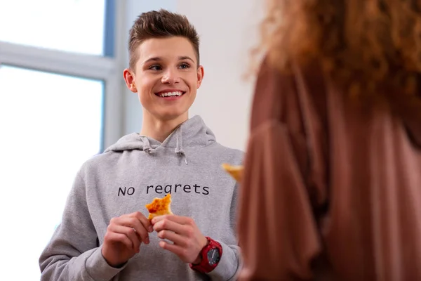 Guapo adolescente sosteniendo pedazo de pizza mientras come con chica rizada —  Fotos de Stock