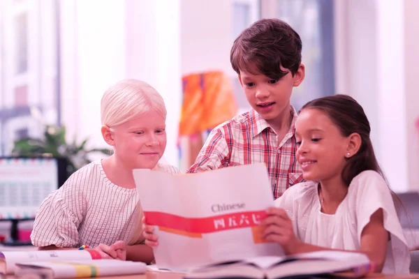 Três crianças em idade escolar sorrindo olhando para caderno de trabalho chinês . — Fotografia de Stock