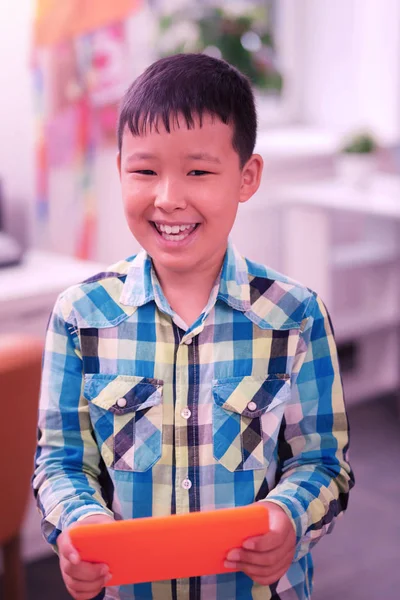 Garçon souriant jouant avec sa tablette orange . — Photo