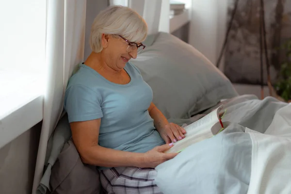 Lächelnde strahlende Dame, die glücklich ein Buch im Bett liest. — Stockfoto