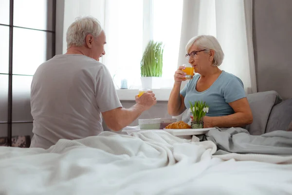 Glückliche Ehepartner frühstücken im Bett und trinken Saft — Stockfoto
