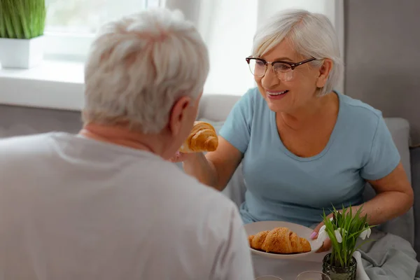 Radostná žena, která krmí svého manžela chutným croissantem. — Stock fotografie
