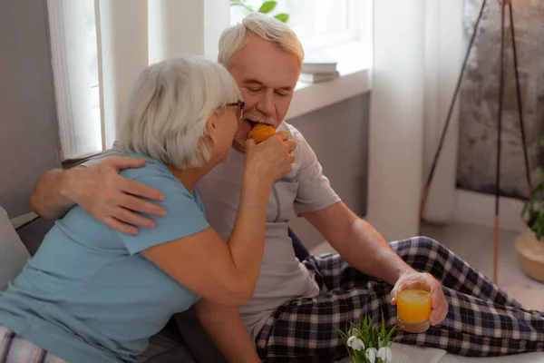 Nice-looking lady feeding up her husband with a freshly-baked croissant