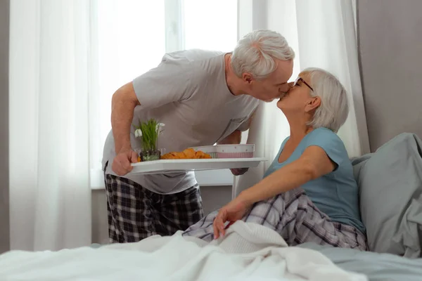 Hombre cariñoso besando a su esposa y sosteniendo bandeja con desayuno — Foto de Stock