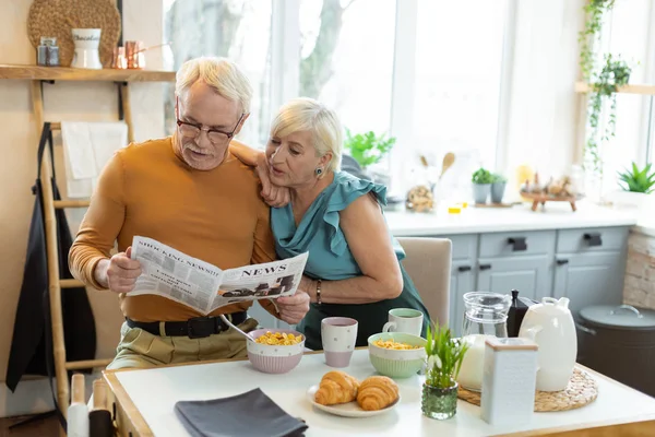 Fókuszált házastársak olvasatban újság ülve a konyhaasztalnál. — Stock Fotó