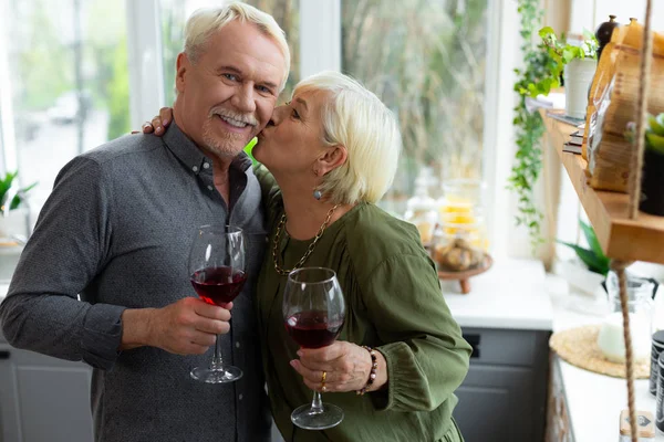 Charming female tenderly kissing her aged white-haired stylish attractive husband